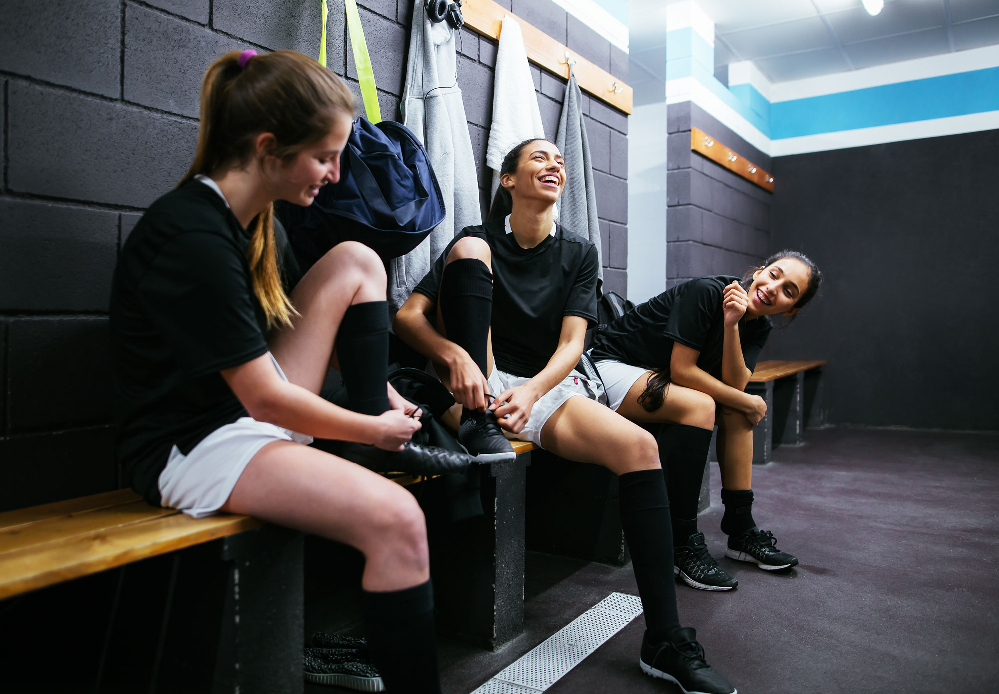 Three young athletes lacing up their shoes in the locker room